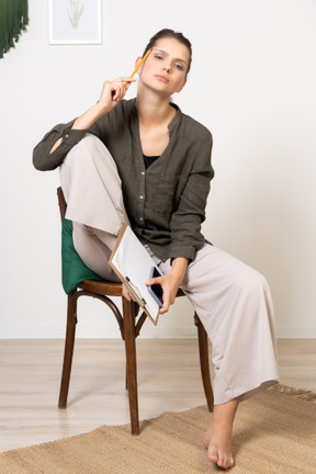 一位体贴的年轻女子穿着家居服坐在椅子上做笔记的前视图