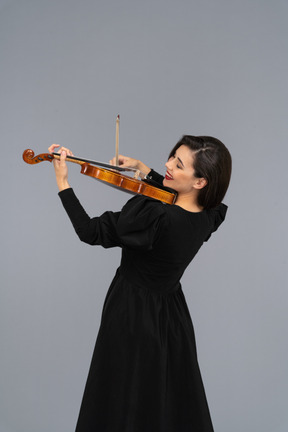 Close-up de uma jovem alegre de vestido preto tocando violino