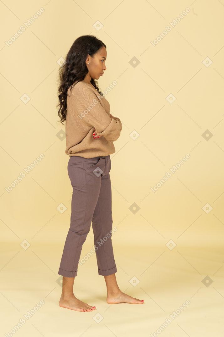 Side view of an offended young dark-skinned female crossing arms
