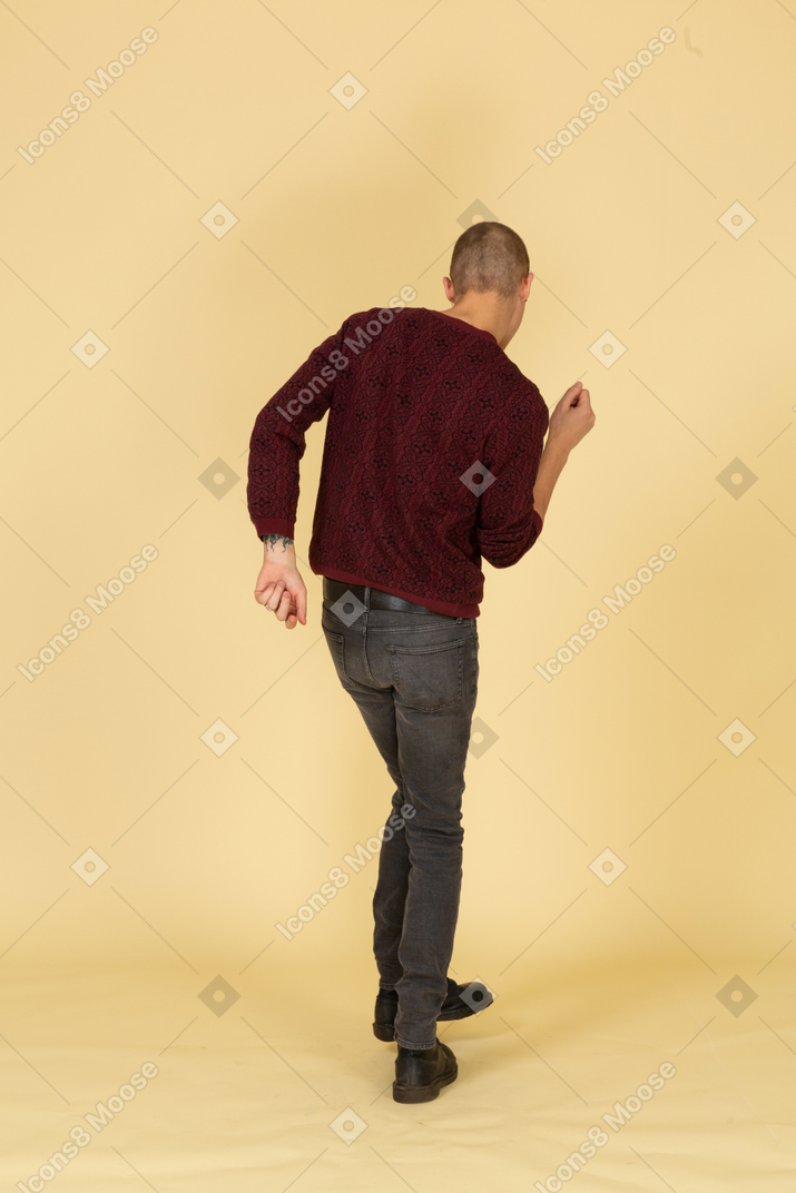 跳舞的年轻男子，穿着红色套头衫抬腿的后视图