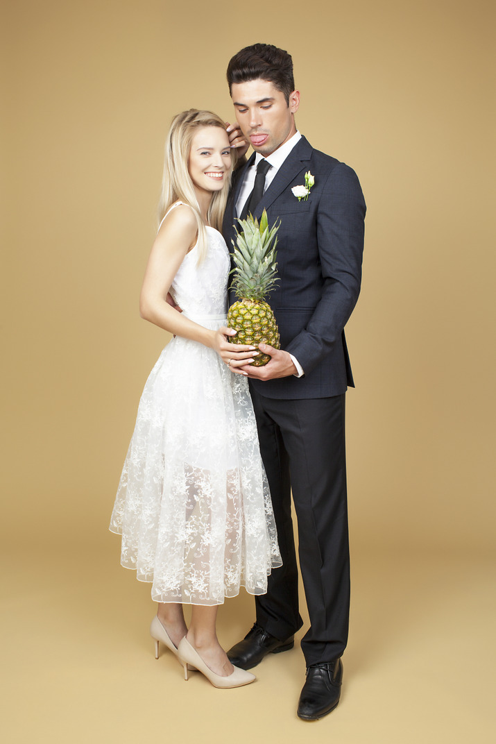 Groom and bride standing close to each other and holding a pineapple