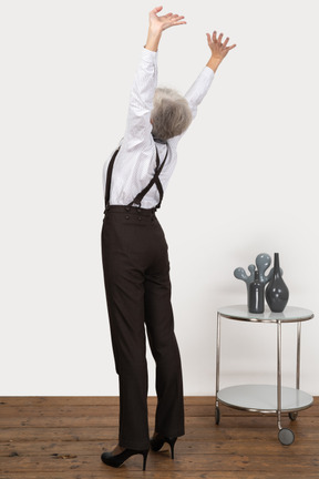 Vue arrière de trois quarts d'une vieille dame en vêtements de bureau en levant les mains