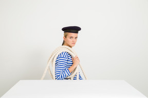 Mujer marinera sentada de perfil con una cuerda por encima del hombro.