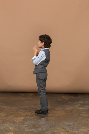 Vista laterale di un ragazzo in giacca e cravatta che fa un gesto di preghiera