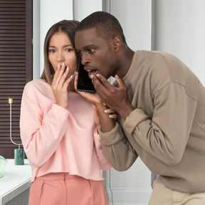 A man and a woman standing next to each other looking shocked while talking on the phone