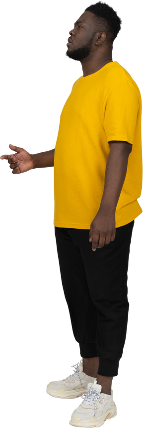Vista de três quartos de um jovem pensativo de pele escura em uma camiseta amarela levantando a mão