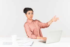 Young indian woman sitting at the office desk and pointing with a hand