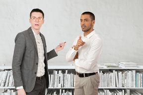 Two men standing next to each other in front of a bookshelf