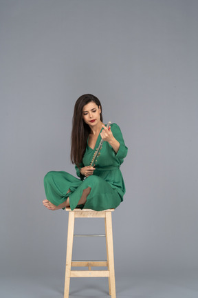 A figura intera di una giovane donna che tiene il clarinetto seduta con le gambe incrociate su una sedia di legno