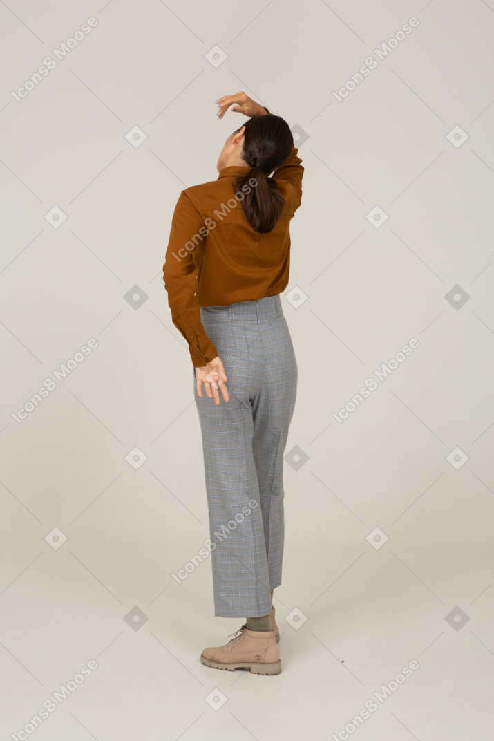 一位身着马裤和衬衫的年轻亚洲女性举手倾斜头的四分之三后视图