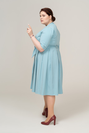 Вид сбоку на женщину в синем платье, указывая пальцем вверх