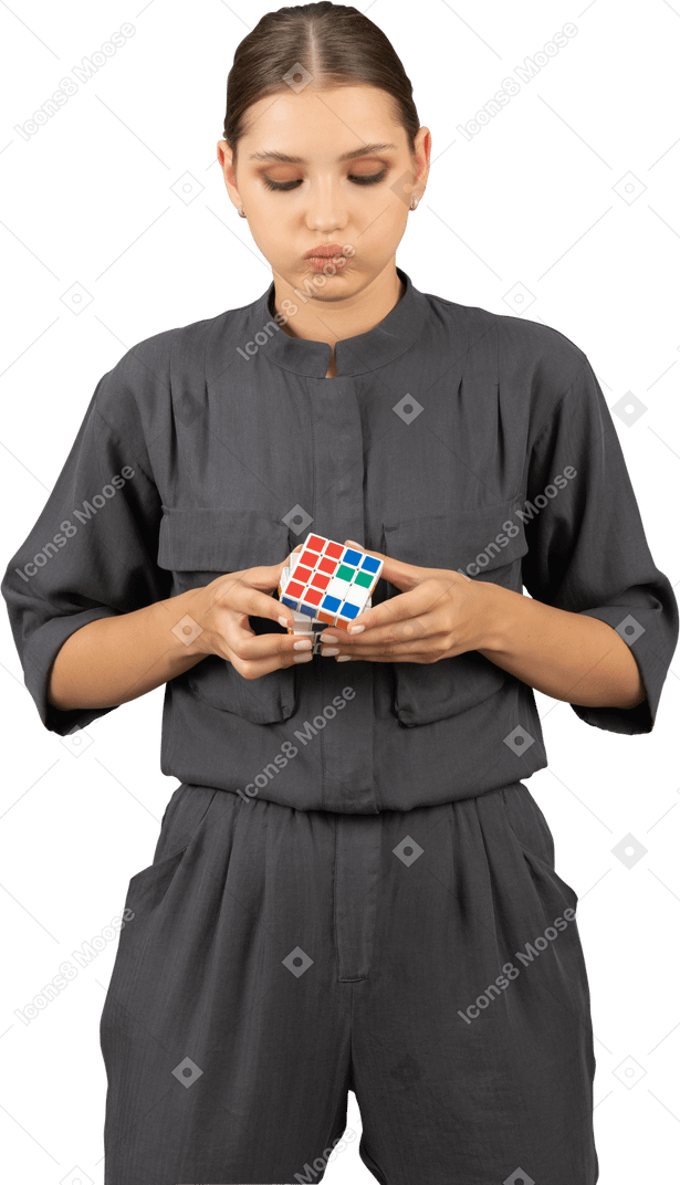 Front view of young woman in a jumpsuit trying to solve the rubik's cube puzzle