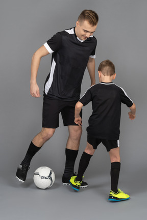 一个年轻男子教小男孩如何玩足球的全长