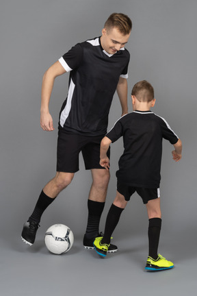 In voller länge von einem jungen mann, der einem kleinen jungen beibringt, wie man fußball spielt