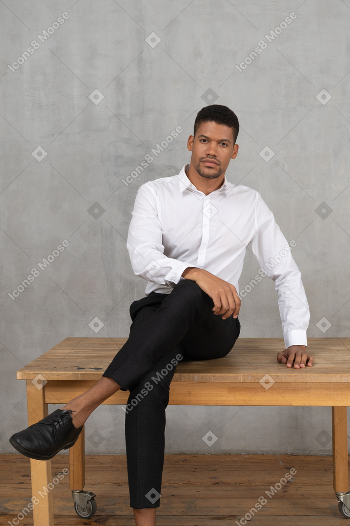 Uomo sicuro di sé in abiti formali seduto a gambe incrociate su un tavolo