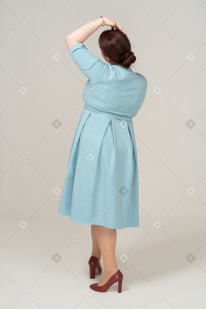 頭に手を置いてポーズをとって青いドレスを着た女性の背面図