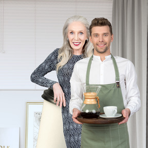 A man and a woman holding a tray with a coffee pot on it