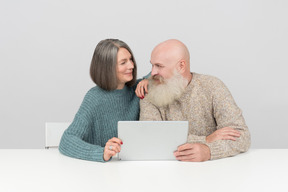 Aged couple sitting at the table and looking at tablet