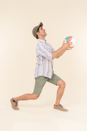 Young caucasian guy standing in profile and holding ball