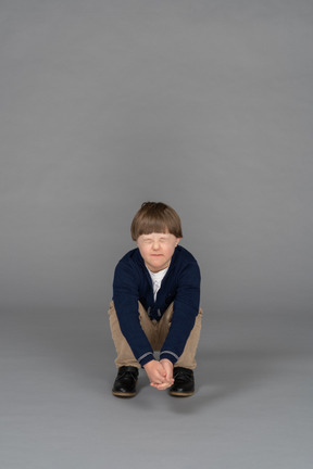 Маленький мальчик сидит на корточках с закрытыми глазами, выглядя испуганным