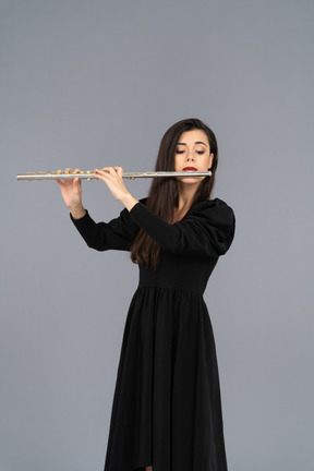 Vista frontale di una giovane donna seria in abito nero che suona il flauto