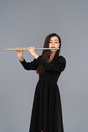 Front view of a serious young lady in black dress playing the flute