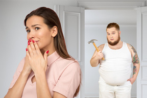 A scared looking woman standing with a man holding a hammer behind her