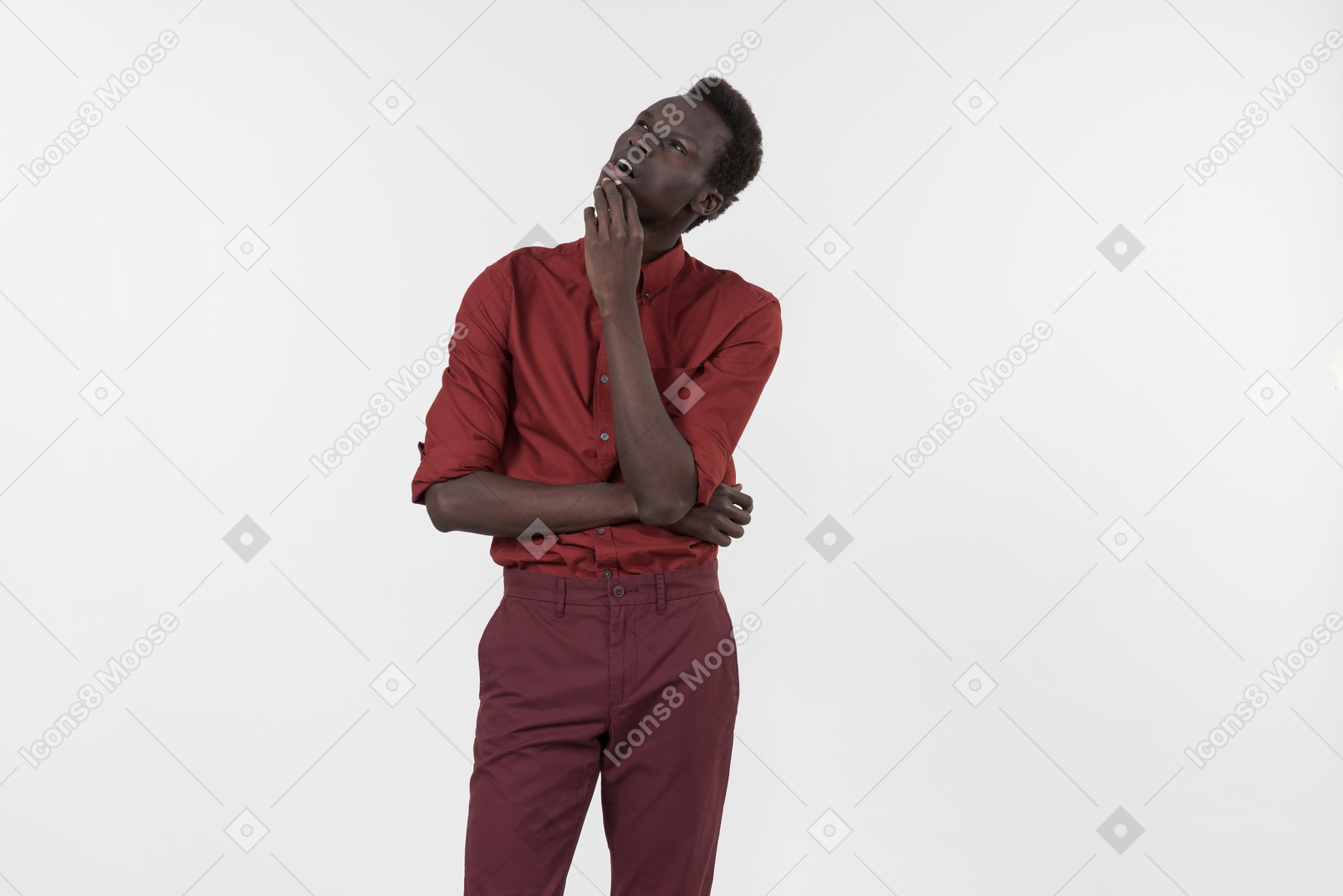 A young black man in a red shirt with rolled up sleeves and dark red pants standing alone on the white background