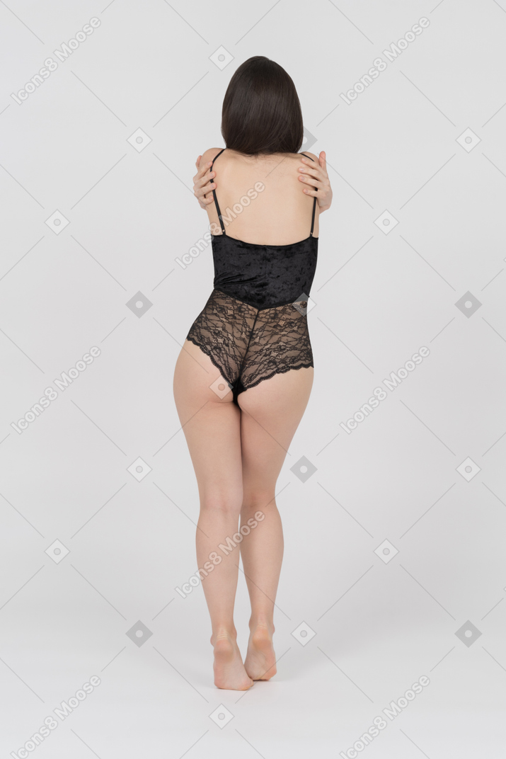 Unrecognizable female in black lace bodysuit embracing herself back to camera