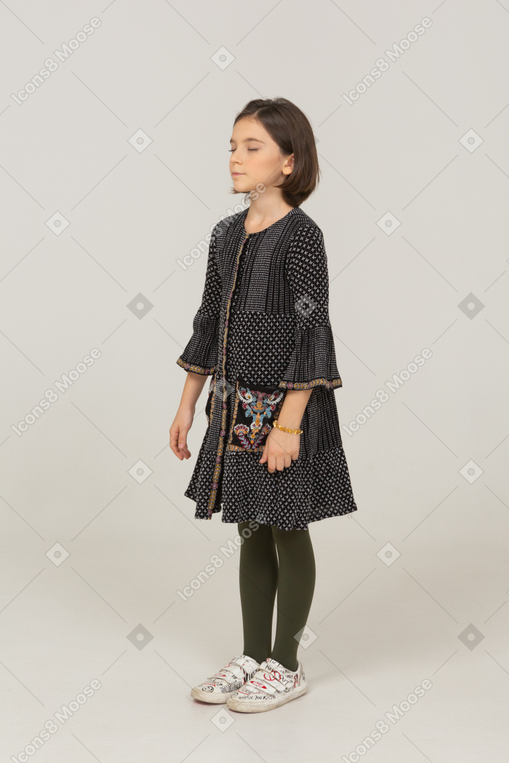 Vista de tres cuartos de una niña vestida de pie con los ojos cerrados