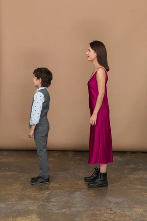 Stylsih mujer en vestido rojo y niño en traje chaleco de pie en el perfil