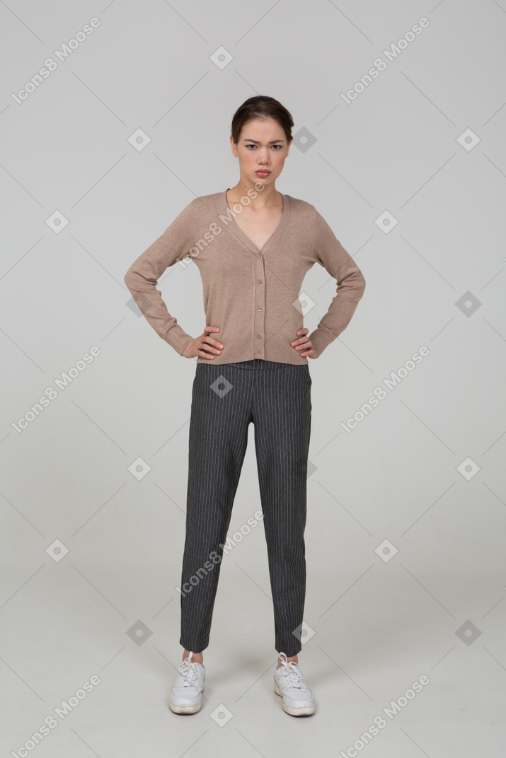 Front view of an angry young lady in pullover and pants putting hands on hips