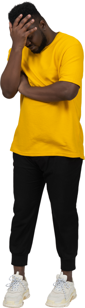 Front view of an ashamed young dark-skinned man in yellow t-shirt hiding face