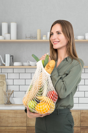 A woman holding a bag full of vegetables in the kitchen