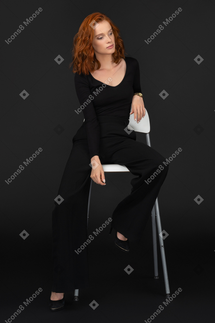 A frontal view of the cute woman dressed in black and sitting on the tall grey chair