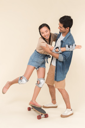 Young caucasian guy teaching asian girl how to skate