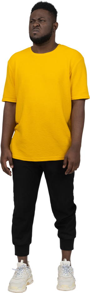 노란색 티셔츠를 입은 불쾌한 얼굴을 찡그린 젊은 검은 피부의 남자의 전면 모습