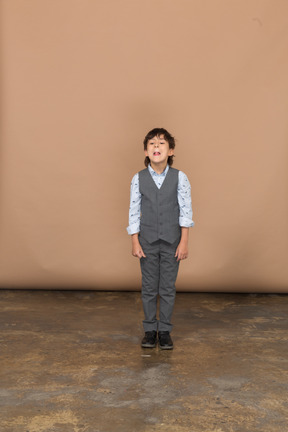 Вид спереди симпатичного мальчика в костюме, смотрящего в камеру и гримасничающего