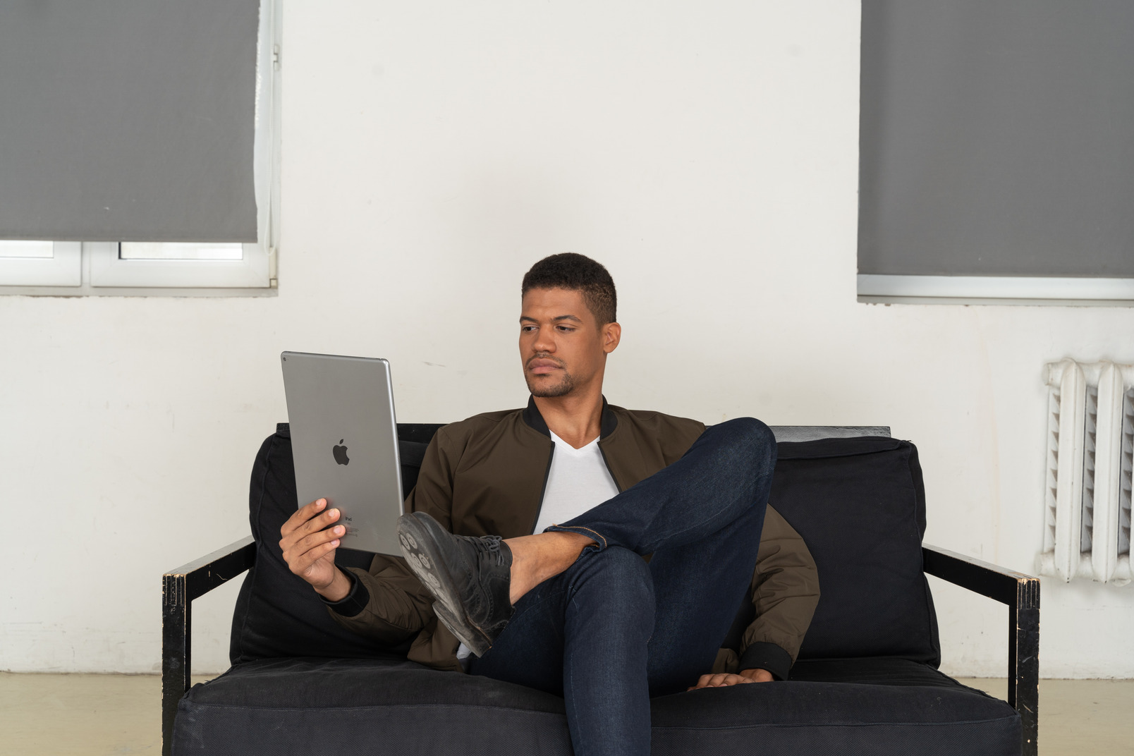 Front view of a bored young man sitting on a sofa while watching the tablet