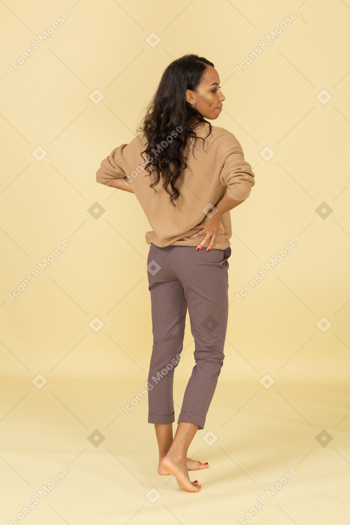 Back view of a dark-skinned female in casual clothes putting hands on hips
