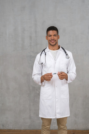 Médecin de sexe masculin souriant tenant un thermomètre