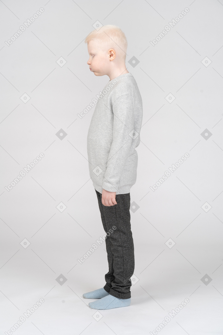 Vista lateral de um garoto loiro em roupas casuais, soprando nas bochechas com os olhos fechados