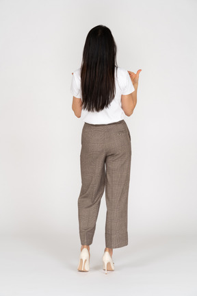 Vista posteriore di una giovane donna in calzoni e t-shirt alzando la mano