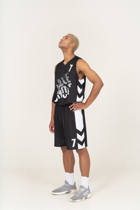 Vue de trois quarts d'un jeune joueur de basket-ball masculin en attente mettant la main sur la hanche