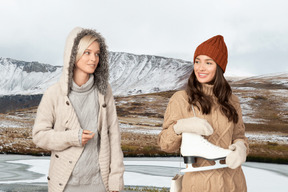 Two young women standing outside and one of them holding ice skates