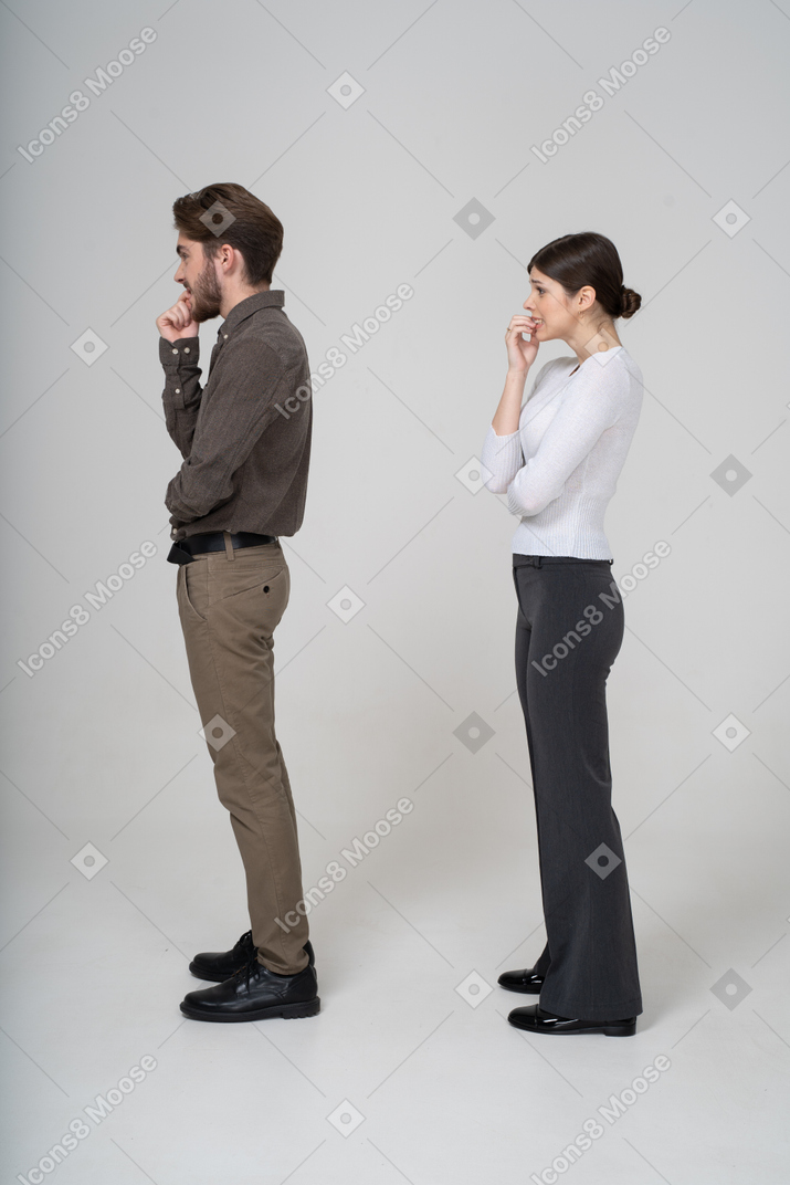 Vista lateral de um jovem casal nervoso com roupa de escritório tocando o queixo