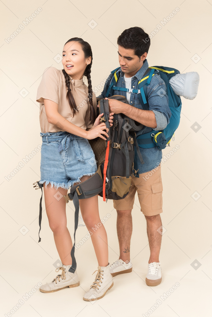 Young man helps taking off backpack to his asian girlfriend