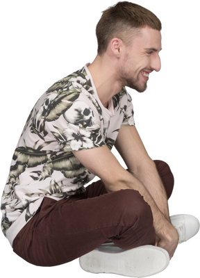 Vista lateral de um homem sentado de pernas cruzadas no chão e rindo