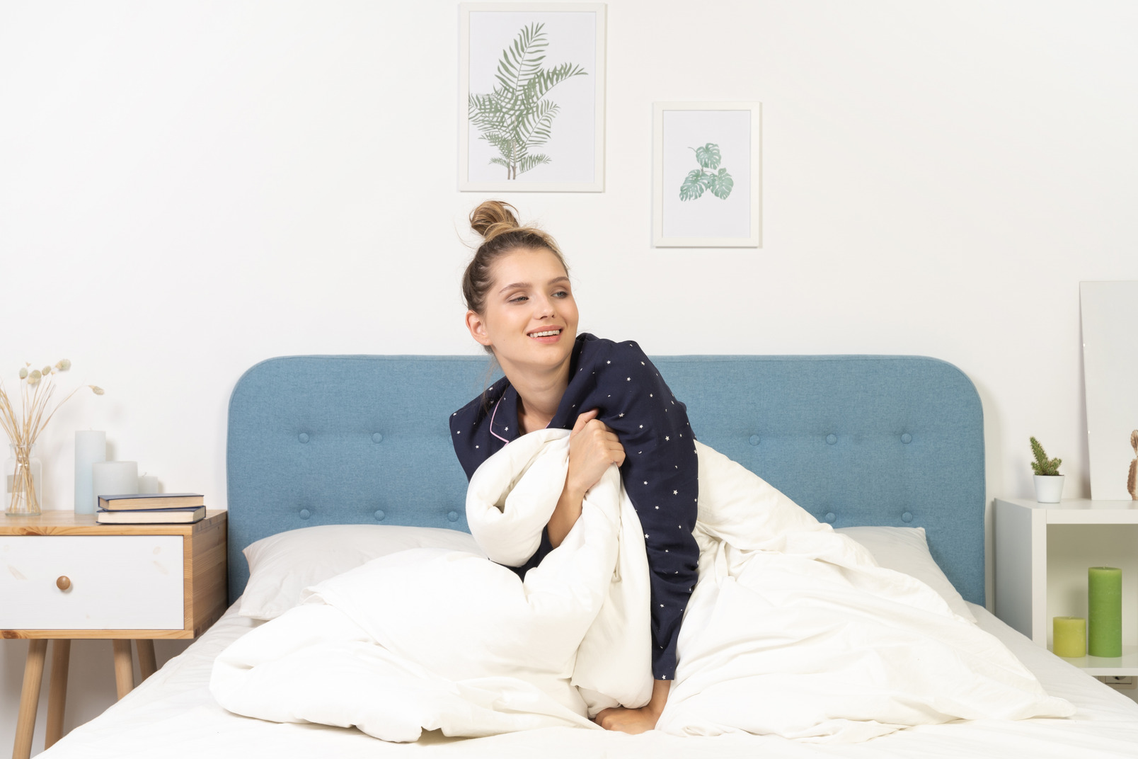 Front view of a smiling young woman in pajamas with blanket staying in bed