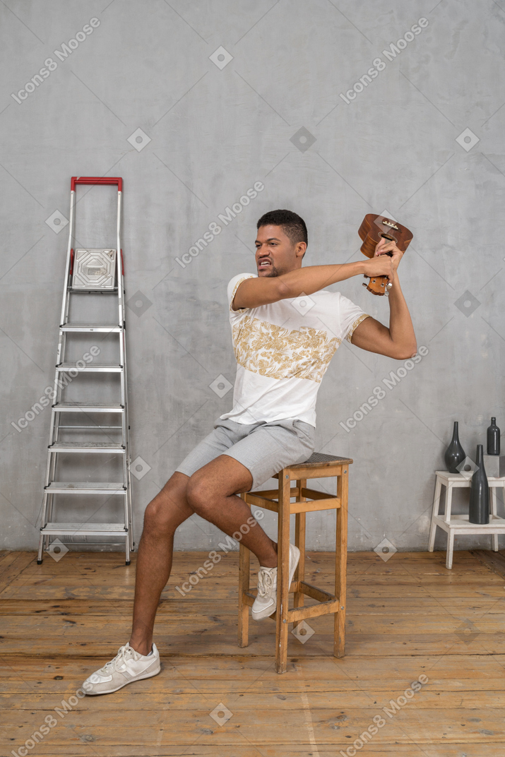 Three-quarter view of a man on a stool swinging an ukulele furiously